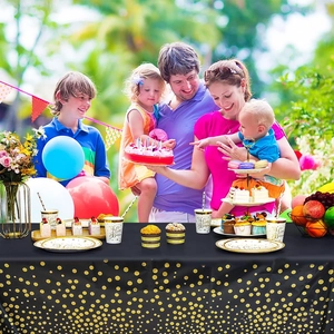 Outdoor birthday party setting featuring black and gold polka dot tableware and tablecloth