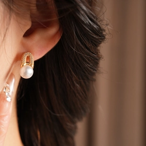 Gros plan d'une boucle d'oreille en perle plaquée or avec zircons portée par un mannequin