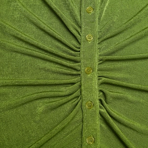 Detail eines grünen Strickoberteils mit Knopfverschluss und eleganter Raffungstextur