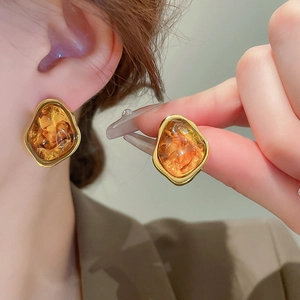 Close-up of vintage amber resin earrings with a gold metal frame on a female ear
