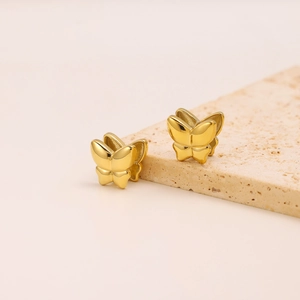 Macro view of gold butterfly stud earrings on beige porous stone display