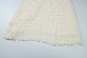 Vue détaillée de la texture du tissu plissé blanc crème sur l'ourlet d'une robe d'été