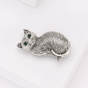 Retro silver cat brooch with green gem eyes shown on a clean white display stand