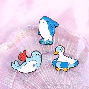 Detail of cute enamel pins featuring blue shark, seal, and duck on an iridescent tray