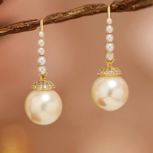 Macro detail of long pearl drop earrings with gold hooks and micro-set zircon accents