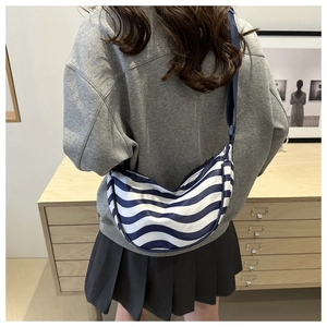 Detail of blue and white wavy striped crescent bag shown on a model in a casual setting