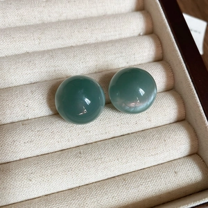 Macro shot of candy-colored emerald green round stud earrings on beige velvet tray