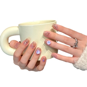 Sparkly pink cat eye press-on nails with blue gems and sequins on a ceramic cup