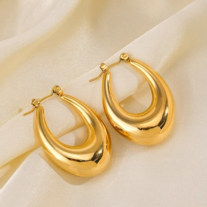Chic golden U-shaped hollow oval hoop earrings on beige silk fabric background