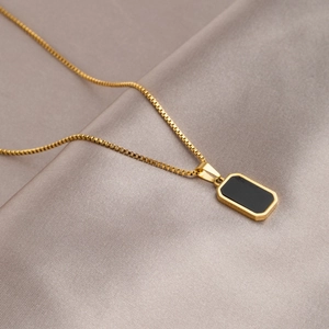Detail of a minimalist gold box chain necklace with a black rectangular pendant on satin