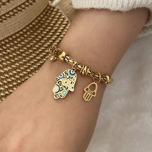 Detail of golden Hamsa Hand bracelet featuring blue enamel evil eye and beaded chain