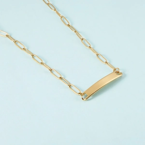 Detailed view of golden paperclip chain with a rectangular polished metal pendant