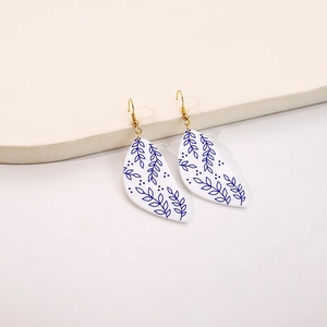 Detail of leaf-shaped acrylic earrings with blue floral patterns and gold hooks
