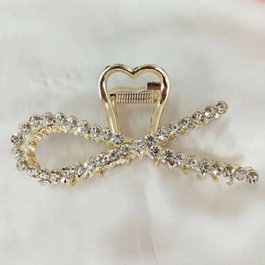 Detail of elegant gold metal hair claw clip featuring a rhinestone bow design for styling