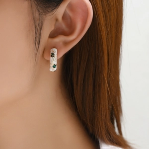 Macro view of vintage white enamel flower hoop earrings with intricate gold floral details