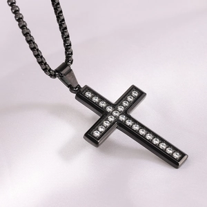 Close-up of black stainless steel cross pendant with white zircon on white silk background