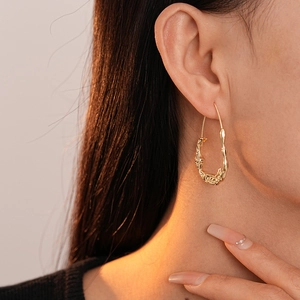 Macro shot of gold irregular wrinkled oval hoop earring worn on a model with warm lighting