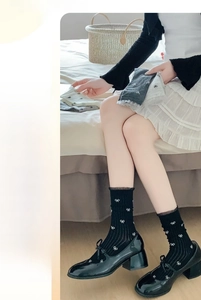 Detail of sheer black mid-calf socks with white bows and lace ruffled edges on feet