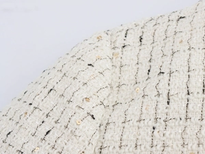 Détail du tissu en tweed blanc avec des fils noirs et dorés et des paillettes brillantes