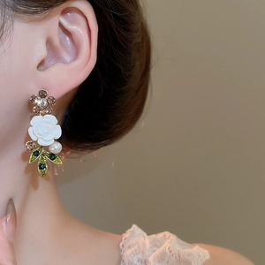 Close-up of floral pendant featuring white rose, crystal petals, pearl, and green leaves