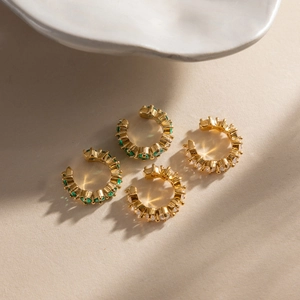 Detail view of four gold-plated ear cuffs with green and white cubic zirconia stones