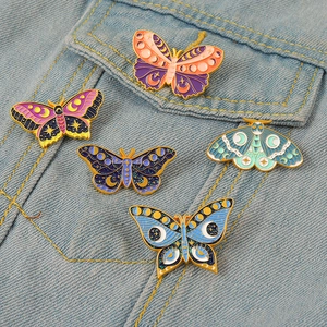 Detail of five mystic butterfly enamel pins with moon and star patterns on denim