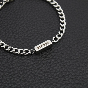 Macro detail of silver stainless steel chain bracelet with always engraving on leather