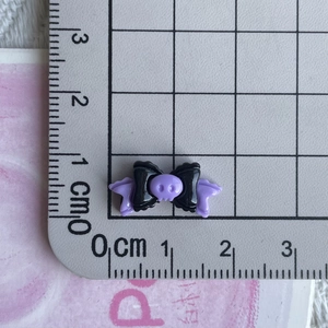 Macro shot of a black and purple skull bow resin accessory with a metric ruler for scale