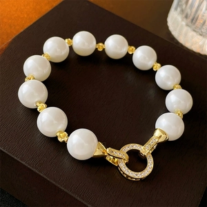 Elegant gold plated pearl bracelet with zircon encrusted round clasp on wooden stand