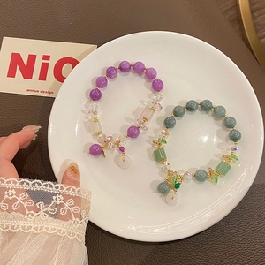 Detail of purple and green beaded bracelets with jadeite charms on a white ceramic plate