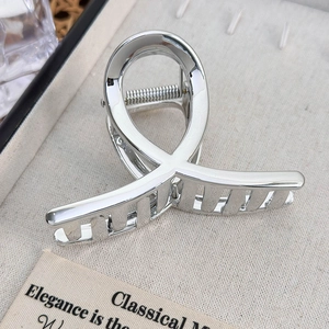 Close-up of a silver shark hair claw clip with a polished finish on a textured display tray