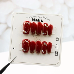 Macro detail of red coffin nails with gold brushstrokes and pearl accents on white display