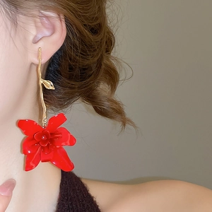 Detailed close-up of a large red floral earring with a golden metallic branch on a model