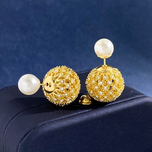 Macro view of gold pearl earrings with hollow pave crystal balls on navy box