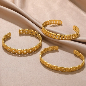 Three gold stainless steel open bangles with woven and chain patterns on champagne silk