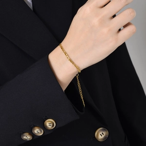 Detail of adjustable 18K gold Figaro chain bracelet on wrist with black blazer background