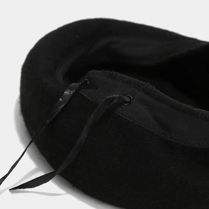 Detail view of black wool beret featuring adjustable ribbon ties and soft texture