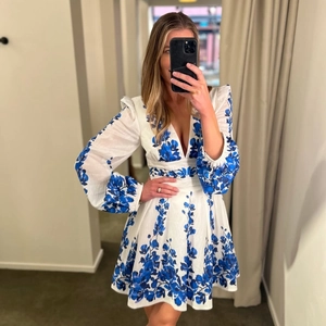 Detail of white long-sleeved dress with deep V-neck and blue floral pattern print