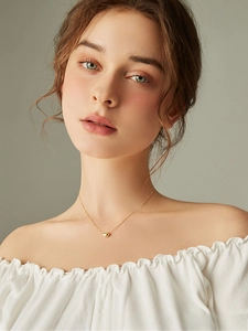 Close-up of golden bean pendant necklace on model with minimalist clavicle chain