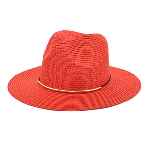 Detail view of red straw fedora hat featuring black rope trim and golden metal accent piece