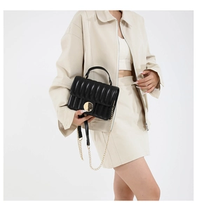 Detail of black quilted leather shoulder bag with gold metal clasp and chain strap