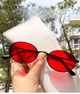 Detail einer Retro-Oval-Sonnenbrille mit roten Gläsern vor einem weißen Lederbeutel