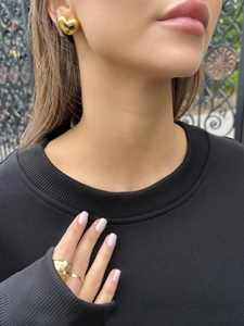 Close-up of gold heart earrings and irregular ring worn by a model in nature