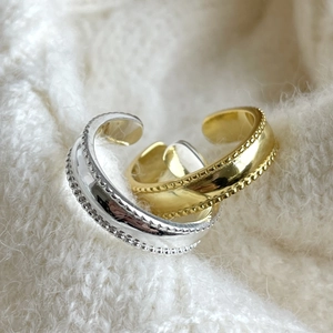 Macro shot of gold and silver adjustable rings with beaded edges on white knitwear