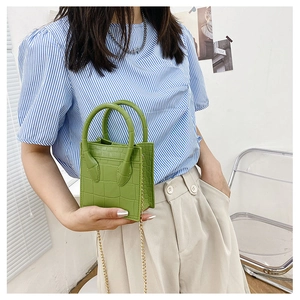 Detail of a green crocodile pattern mini handbag with gold chain strap held by model