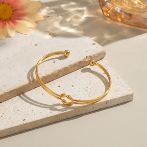 Close-up of gold knotted open bangle on stone surface with elegant light reflections