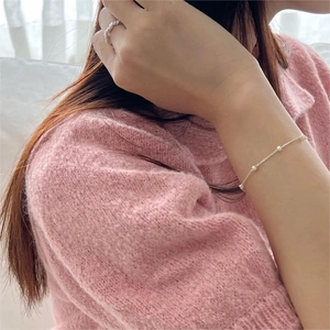 Detail of S925 silver pearl bracelet and twisted ring worn on a pink knitted sleeve