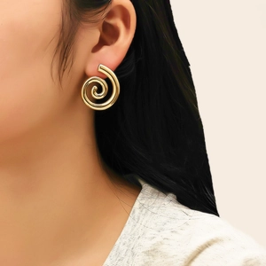 Détail de boucles d'oreilles spirales dorées portées par un mannequin sur fond neutre