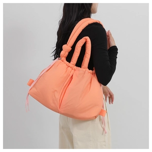 Detail of orange nylon shoulder bag featuring puffy quilted design and knotted strap