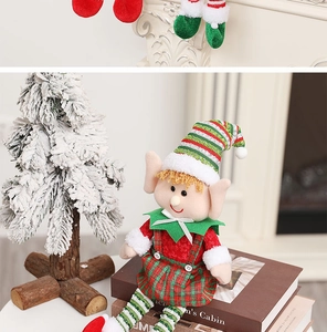 Close-up of a Christmas elf doll in plaid dress next to a mini snowy tree on a fireplace
